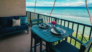 Un balcón con una mesa dispuesta para dos personas, con vista a una playa con palmeras y agua azul cristalina.