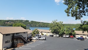 A parking lot with several cars, a building with a staircase, and a view of a lake and hills in the background.