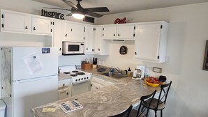 A kitchen with white cabinets, a microwave, a stove, a sink, and a ceiling fan.