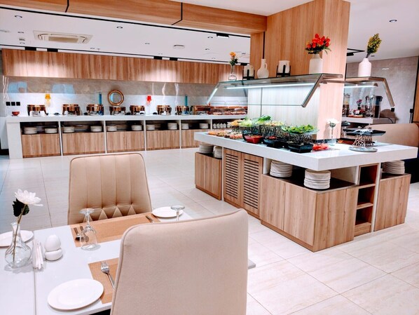 A modern kitchen with wooden cabinets, a central island with food, and a dining area with chairs and a table set for two.