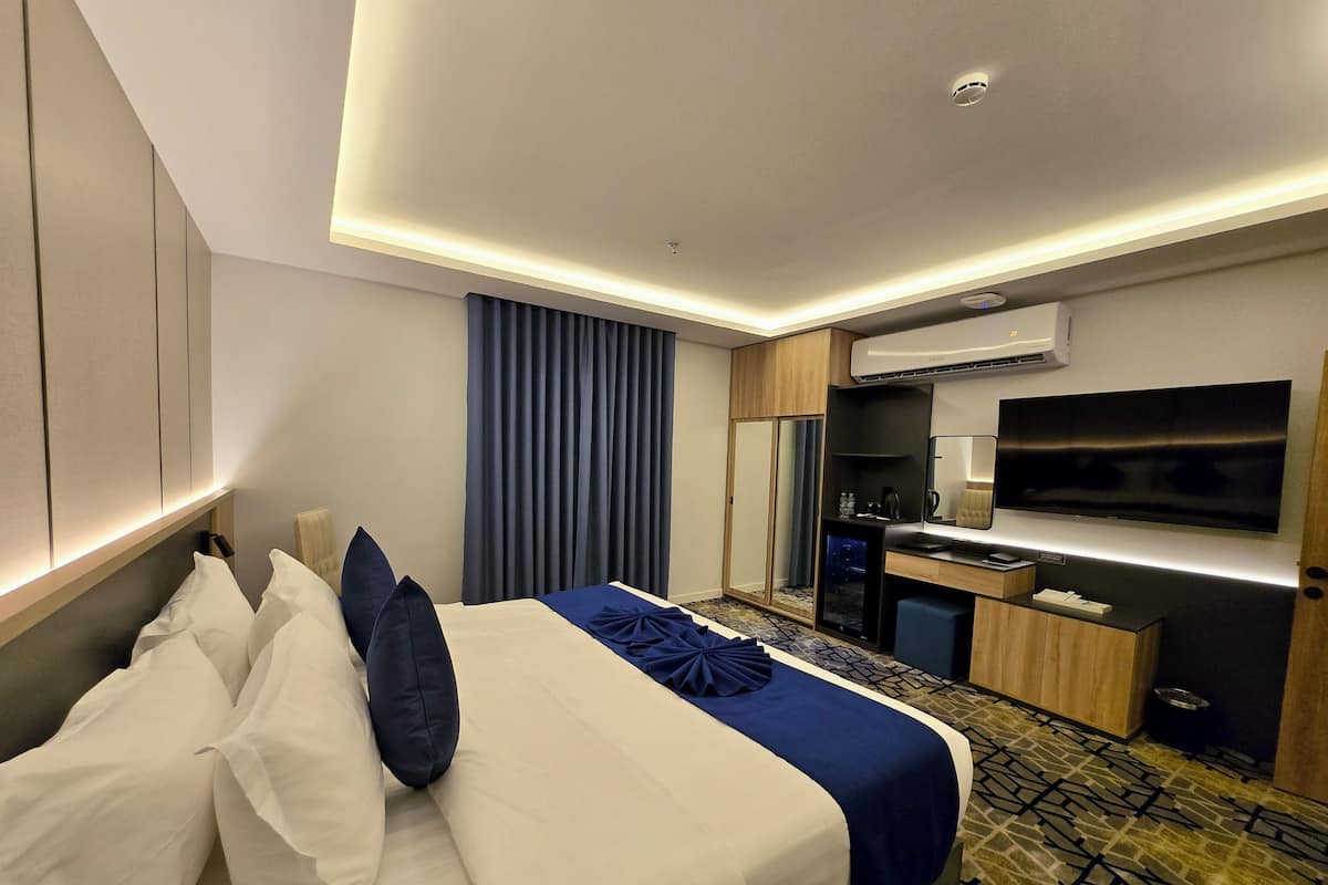A hotel room with a bed, a desk, a television, and an air conditioning unit.