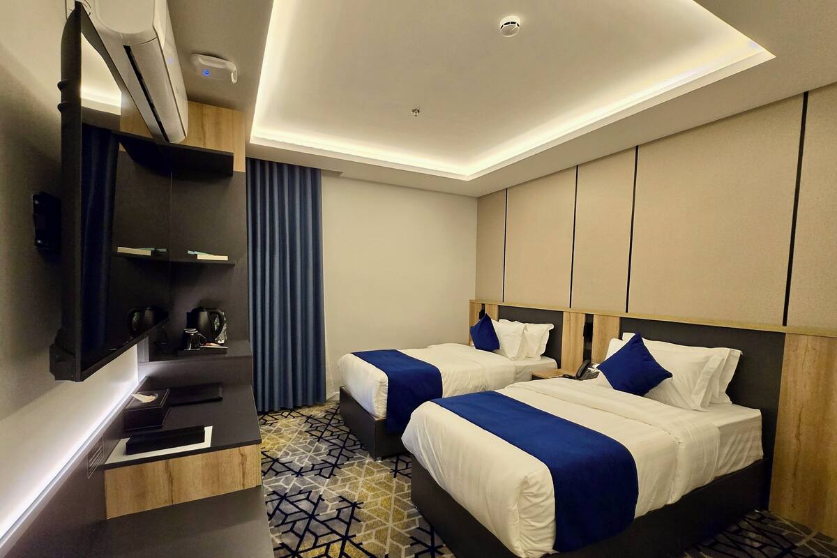 A hotel room with two beds, a desk, a mirror, and a patterned carpet.