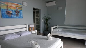 A modern bedroom with a large bed, a smaller bed, a potted plant, and a painting of boats on the wall. - Estudio con vista al oceano (Tola)