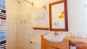 A bathroom with a shower, toilet, sink, and a mirror with a wooden frame. - Apartamento con vista al mar (Tola)