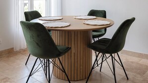A round wooden dining table with four green chairs, a round mirror on the wall, and a window with white curtains. - Le 202 Sainte Ségolène - 1 room, rénovated, heart of Metz (Metz)