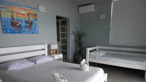 A modern hotel room with a large bed, a smaller bed, a potted plant, and a painting of boats on the wall. - Penthouse con vista al oceano (Tola)