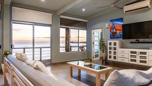 A spacious living room with a large window overlooking the ocean, a comfortable seating area, and a flat-screen TV mounted on the wall. - Penthouse con vista al oceano (Tola)