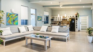 A modern living room with a sectional sofa, a glass coffee table, and a kitchen in the background. - Penthouse con vista al oceano (Tola)