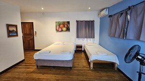 A room with two single beds, a wooden floor, a painting on the wall, an air conditioning unit, and a fan. - Chalet con vista al Océano (Tola)