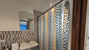 A bathroom with a tiled wall, a sink, and a shower curtain with a geometric pattern. - Chalet con vista al Océano (Tola)