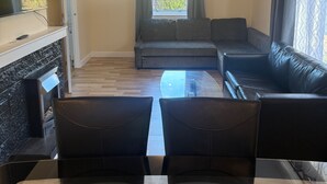 A living room with a fireplace, a sofa, a TV, and a view of the outdoors. - Cozy Kirkcaldy Hideaway - 3br House (Kirkcaldy)