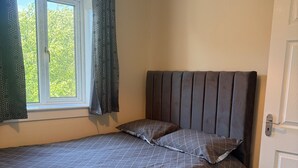 A bedroom with a bed, a window with curtains, a door, and a ceiling light. - Cozy Kirkcaldy Hideaway - 3br House (Kirkcaldy)
