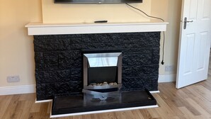 A living room with a fireplace, a mounted TV, and a door. - Cozy Kirkcaldy Hideaway - 3br House (Kirkcaldy)
