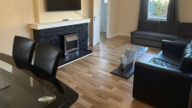 A living room with a flat-screen TV mounted above a fireplace, a sofa, and a glass coffee table. - Cozy Kirkcaldy Hideaway - 3br House (Kirkcaldy)