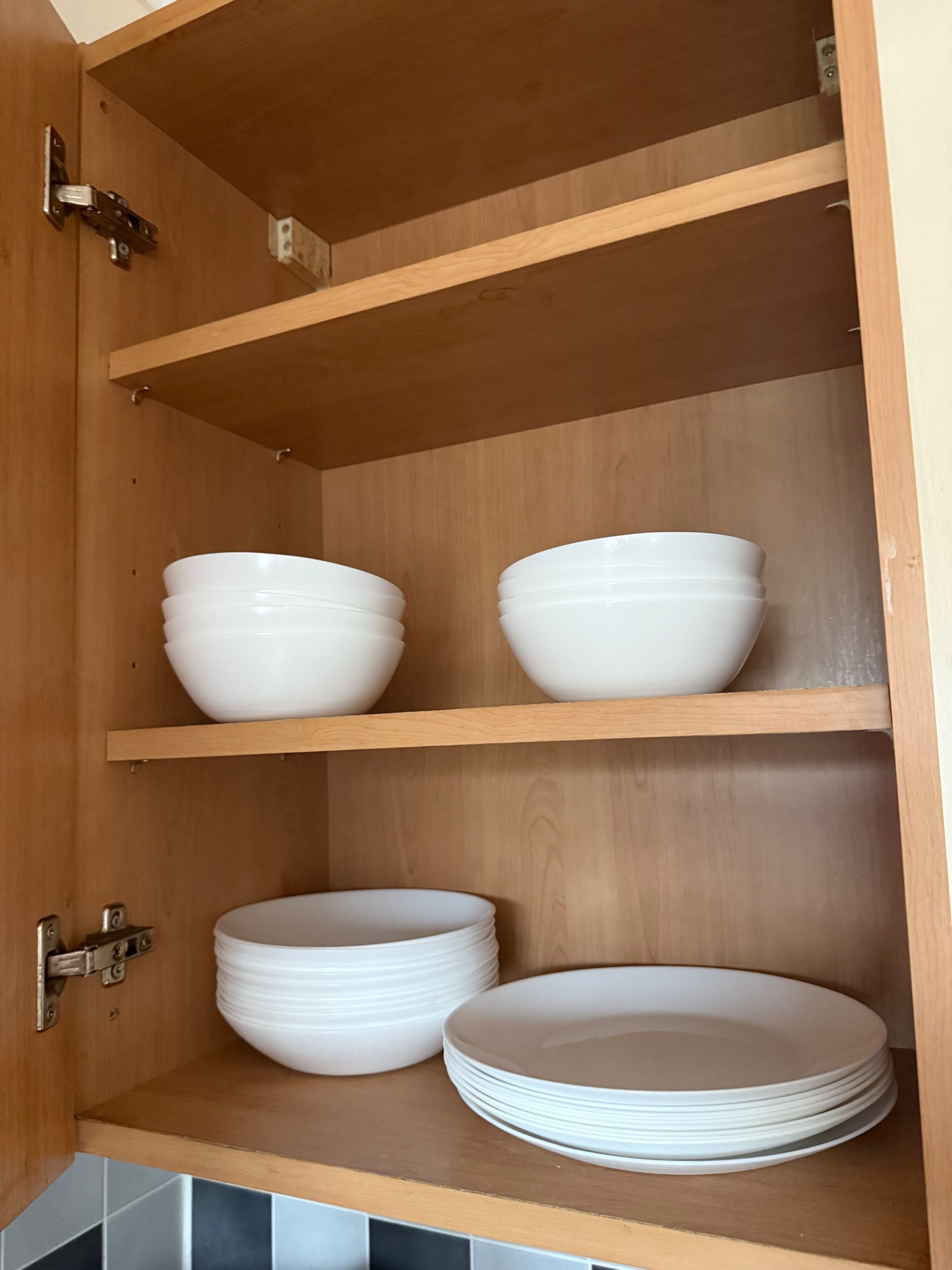 Un armario de madera con estantes que contienen cuencos y platos blancos.