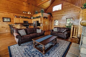 Interior de cabana de toras com sala de estar, área de jantar e cozinha.