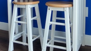 A white wooden table with two stools against a blue wall.