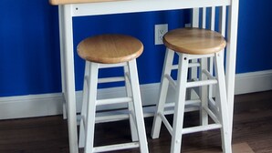 A small white table with two wooden stools against a blue wall.