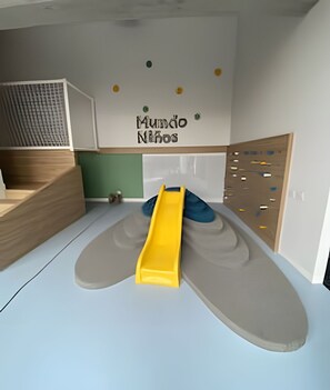 A play area with a slide, a climbing wall, and a wall with colorful dots.