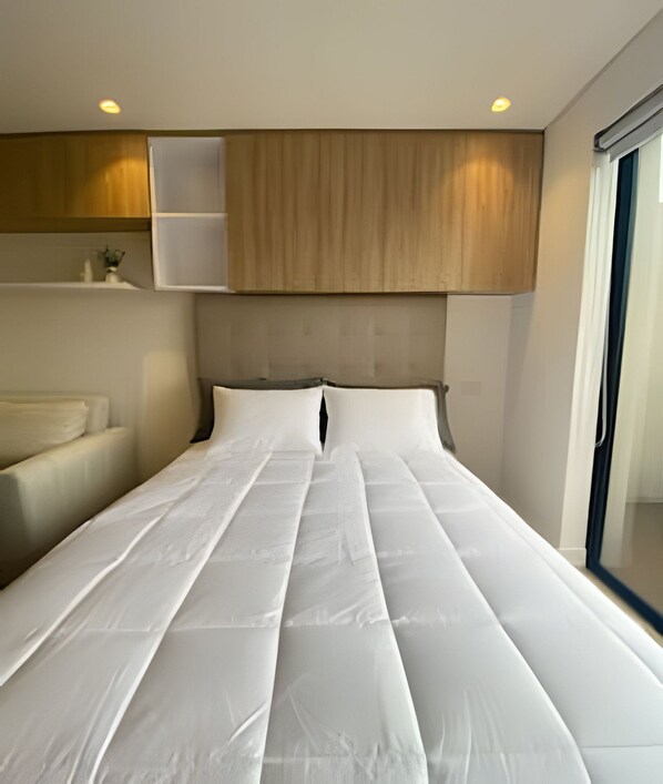 A modern hotel room with a large bed, wooden headboard, and a window with a view.
