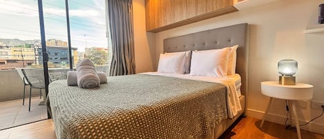 Ein Hotelzimmer mit einem großen Bett, einem Nachttisch mit Lampe, Blick auf die Stadt vom Balkon und modernem Design.
