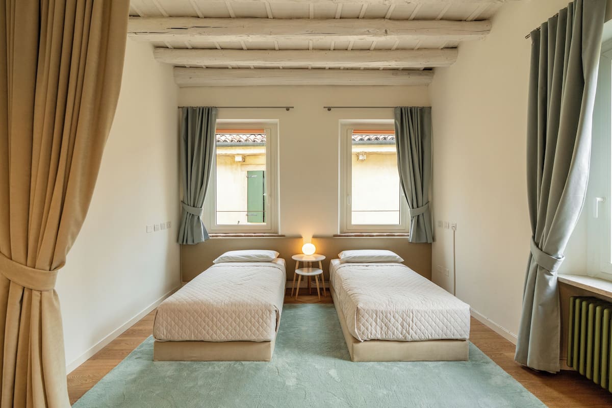 Une chambre avec deux lits, une petite table et une fenêtre avec des rideaux.