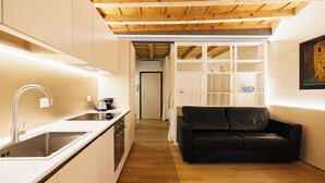 Una cocina compacta con un lavamanos y estufa modernos, un sofá de cuero negro y techo de madera.