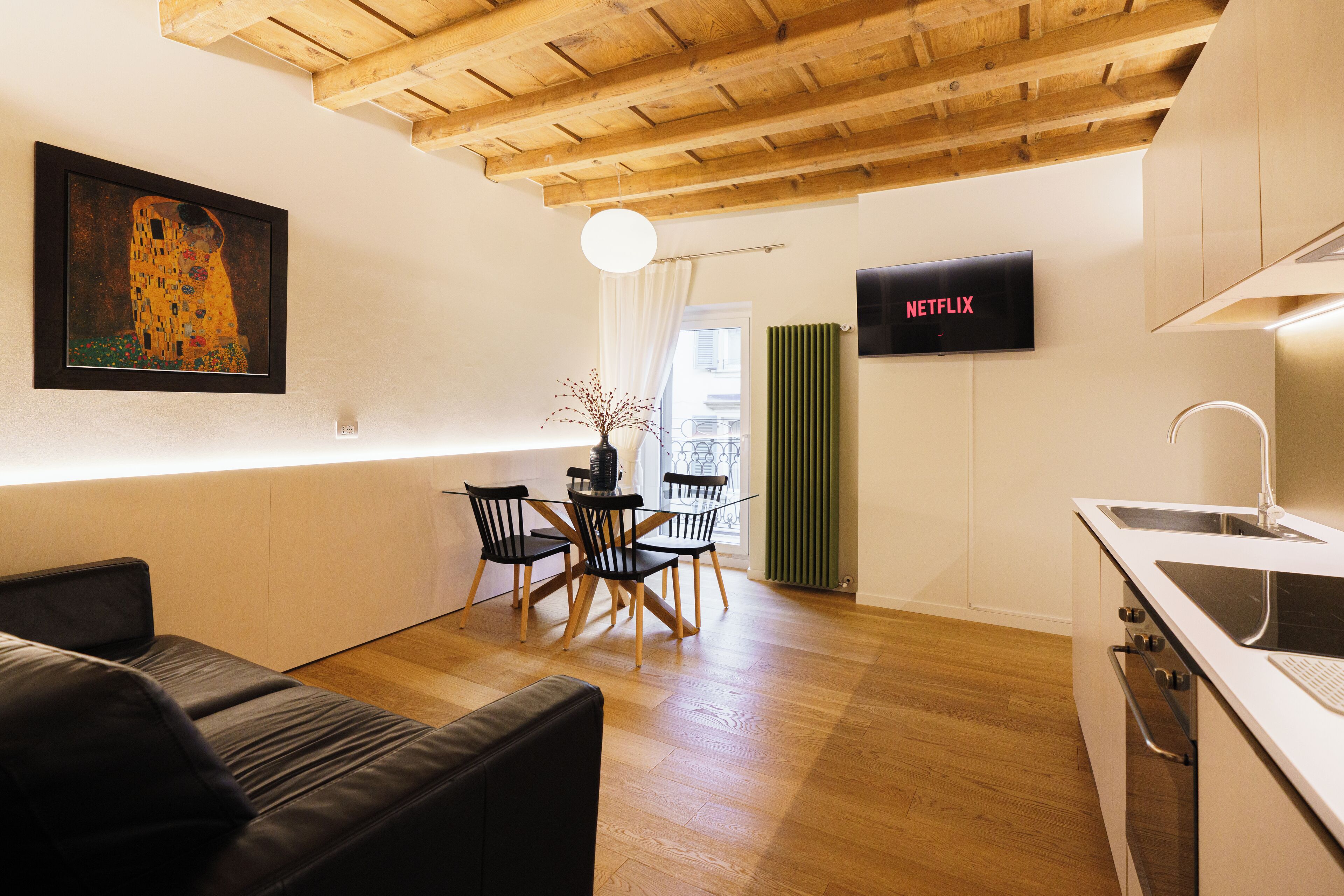 Una cocina moderna con horno empotrado, una zona de comedor con mesa y sillas de madera, y un cuadro en la pared.