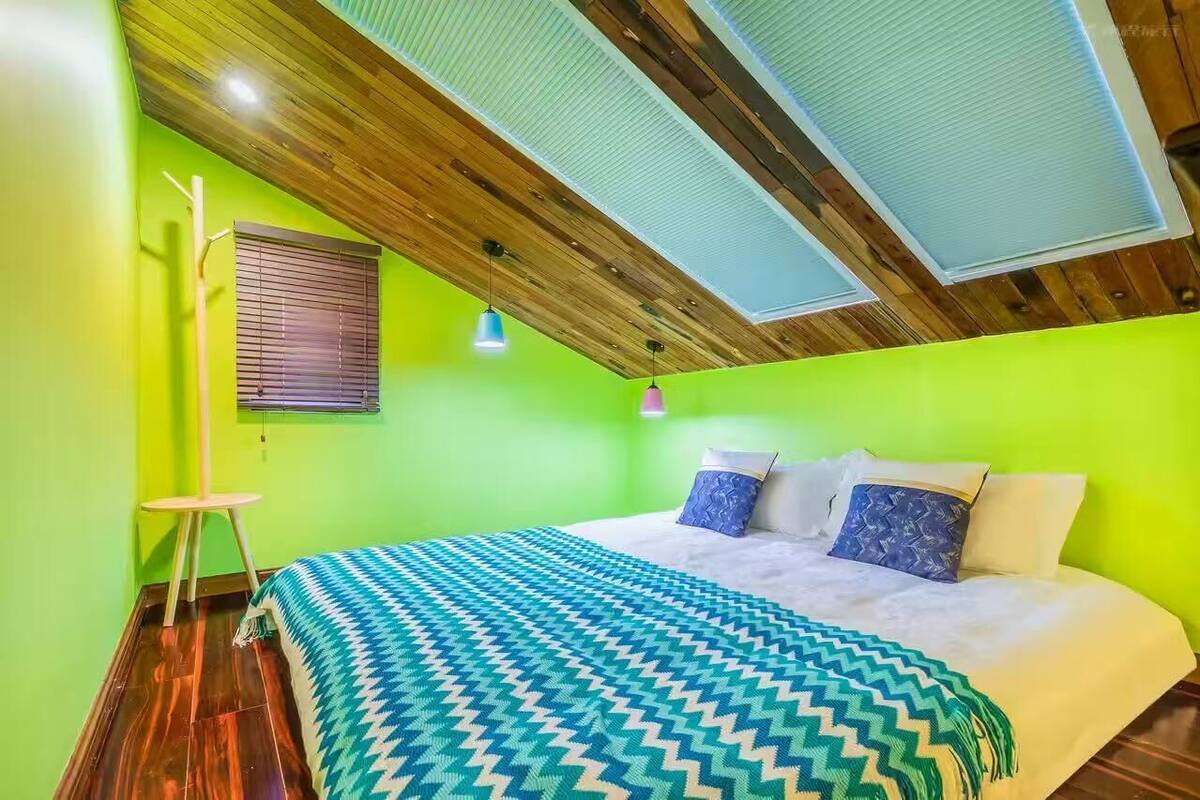 Una habitación con techo de madera, una cama con ropa de cama estampada, una lámpara de pie y una ventana con persianas.