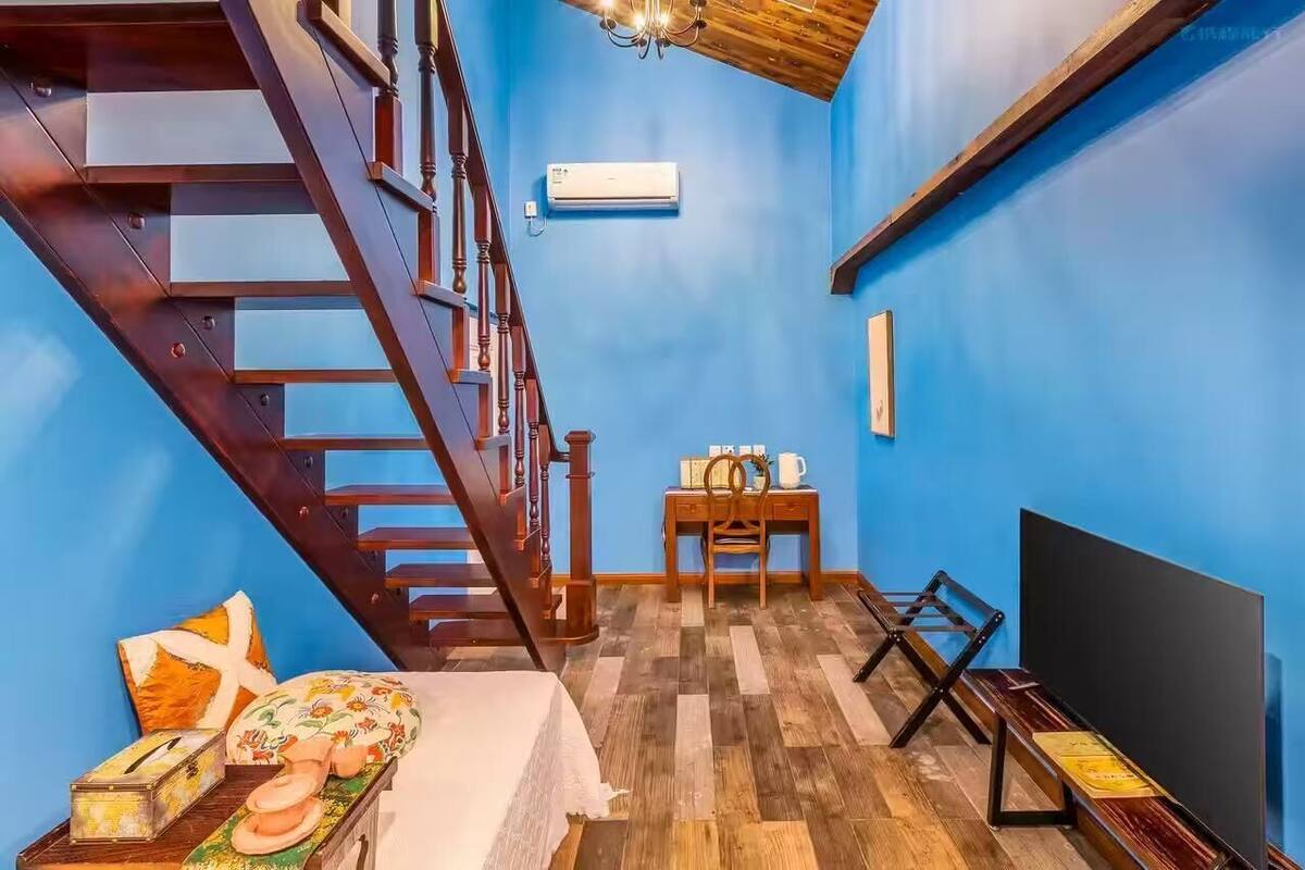 Una habitación con una escalera de madera, una pequeña mesa con sillas, una cama y un televisor de pantalla plana.