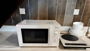A white microwave oven with a digital display and control knobs, placed on a kitchen counter next to a stack of white plates and a black induction cooktop. - Beijing Shixi Inn near Forbidding City (Beijing)