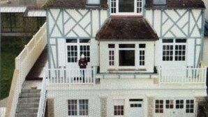 Une maison à deux étages dotée d’un balcon, d’une cheminée et de nombreuses fenêtres.