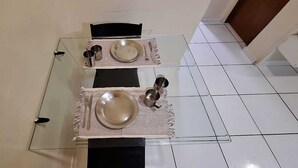 Un tavolo da pranzo apparecchiato con piatti, posate e tazze, su un pavimento piastrellato, circondato da sedie.