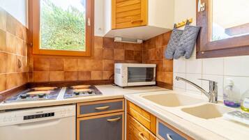 A kitchen with a stove, microwave, sink, wooden cabinets, and a window with a view of greenery.