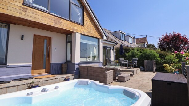 Et moderne hus med jacuzzi, udendørs møbler og en træterrasse.