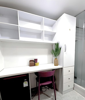Ein modernes Zimmer mit weißem Schreibtisch, violettem Stuhl und einer Duschkabine aus Glas.