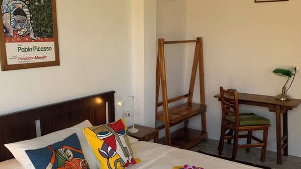 Ett hotellrum med en säng, ett skrivbord, en stol och en väggmonterad luftkonditioneringsanläggning.
