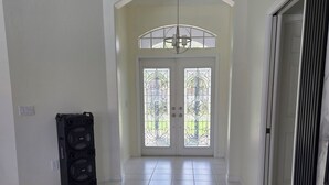 A spacious, well-lit room with a tiled floor, a large arched doorway, and a black speaker unit against the wall.