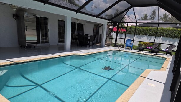 A swimming pool with a clear view of the water, surrounded by a covered patio area with chairs and a table.