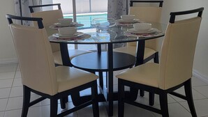 A dining area with a round glass table, six chairs, and a view of a swimming pool and buildings outside.
