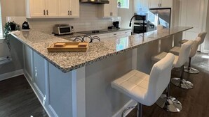 Une cuisine moderne avec des meubles blancs, un comptoir en granit et des tabourets de bar.