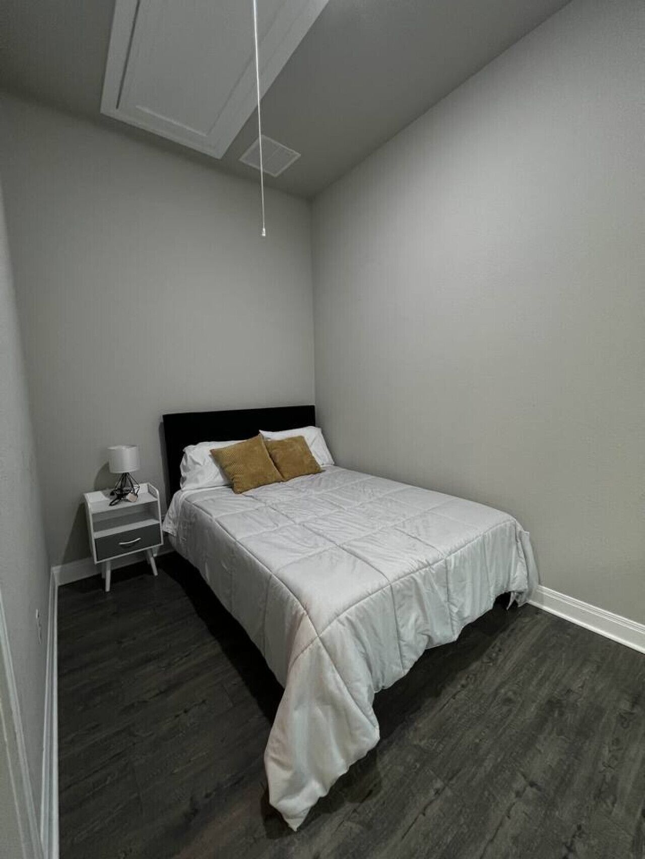 A bedroom with a bed, a nightstand, and a hanging light fixture.
