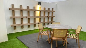 Een terras met een ronde tafel en vier stoelen, omringd door kunstgras en een houten omheining.