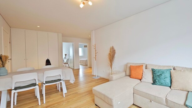 Een moderne woonkamer met een bank, een eettafel met stoelen, en een keuken in de achtergrond.