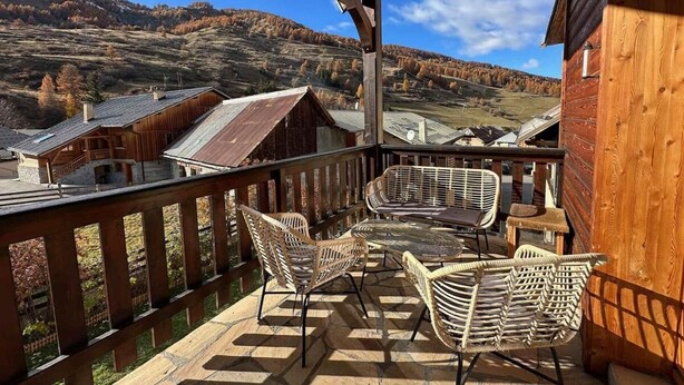 Une terrasse en bois, meublée de mobilier en osier, qui offre une vue sur un paysage montagneux.