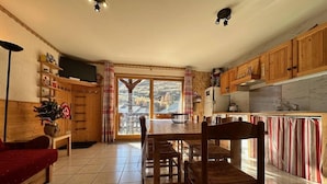 Un salon chaleureux avec un canapé en bois, une table à manger avec des chaises, un téléviseur et un coin cuisine doté de meubles en bois.