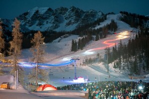 Una stazione sciistica con una seggiovia, una folla di persone e montagne sullo sfondo.