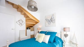 A bedroom with a bed, a nightstand, a lamp, a chair, a wall art piece, and a staircase.