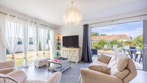 A modern living room with a flat-screen TV, beige sofas, a coffee table, and a large sliding glass door leading to an outdoor area.