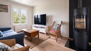 Un salon comprenant un canapé, un téléviseur, un fauteuil en osier et un poêle à bois.